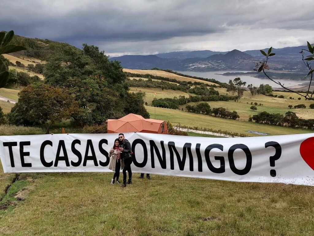 Letrero de "¿Te casas conmigo?" con una pareja al frente en Parapente El Dorado