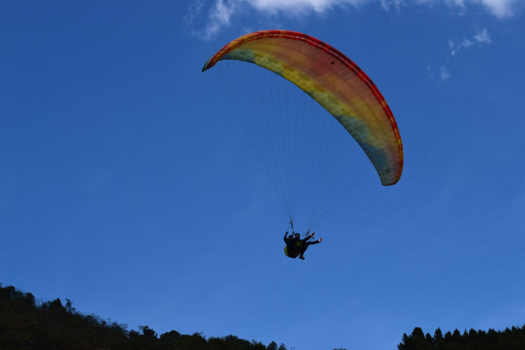 Parapente en el aire con dos personas visto desde un ángulo en contrapicado